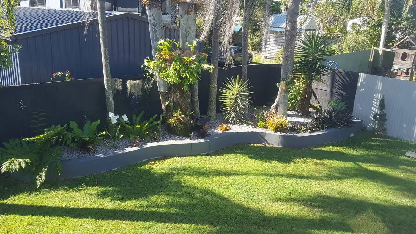 Neatly mown lawn beside a curved garden bed of ferns, bromeliads and palms