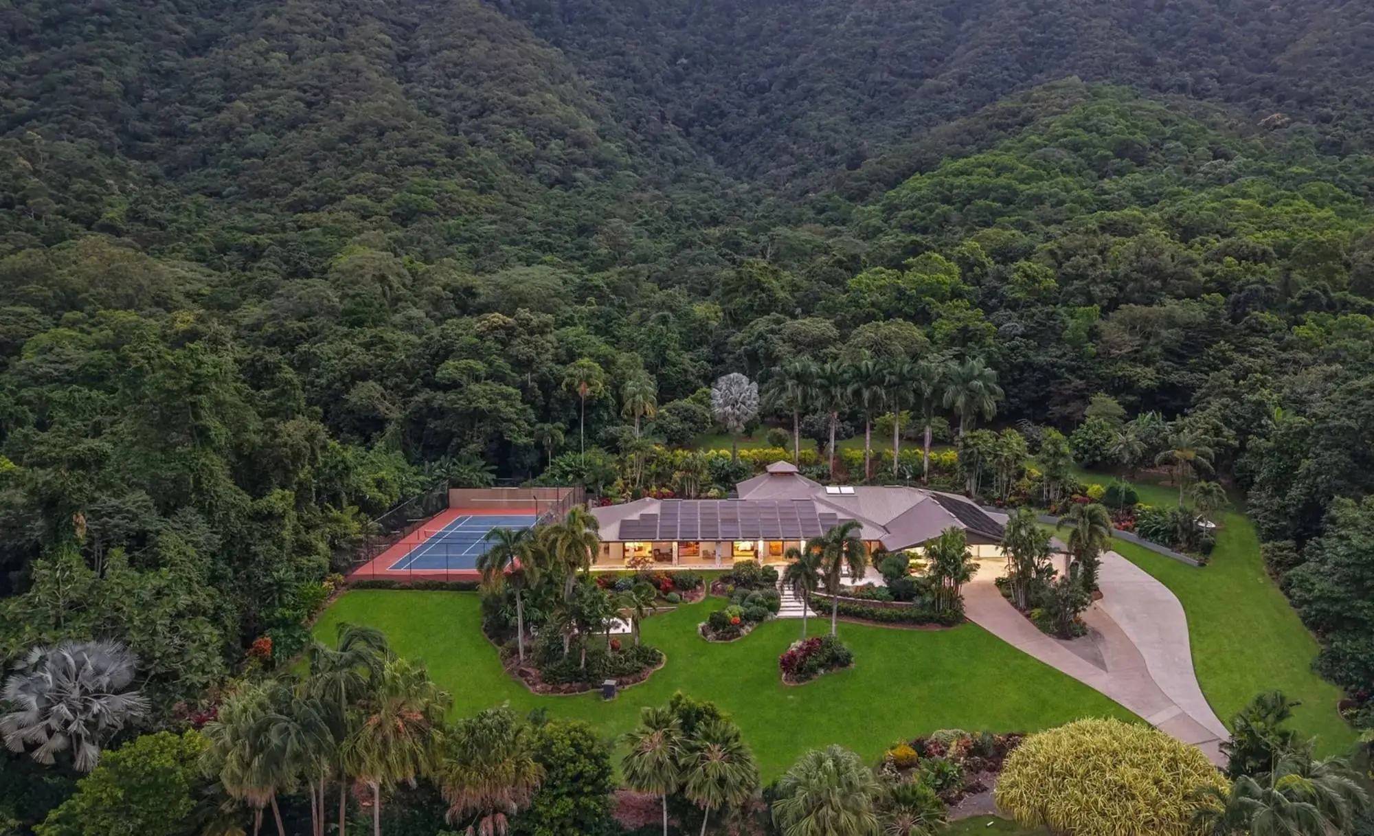Aerial view of a large, freshly mown lawn and tropical gardens at the foot of rainforest-covered hills near Cairns